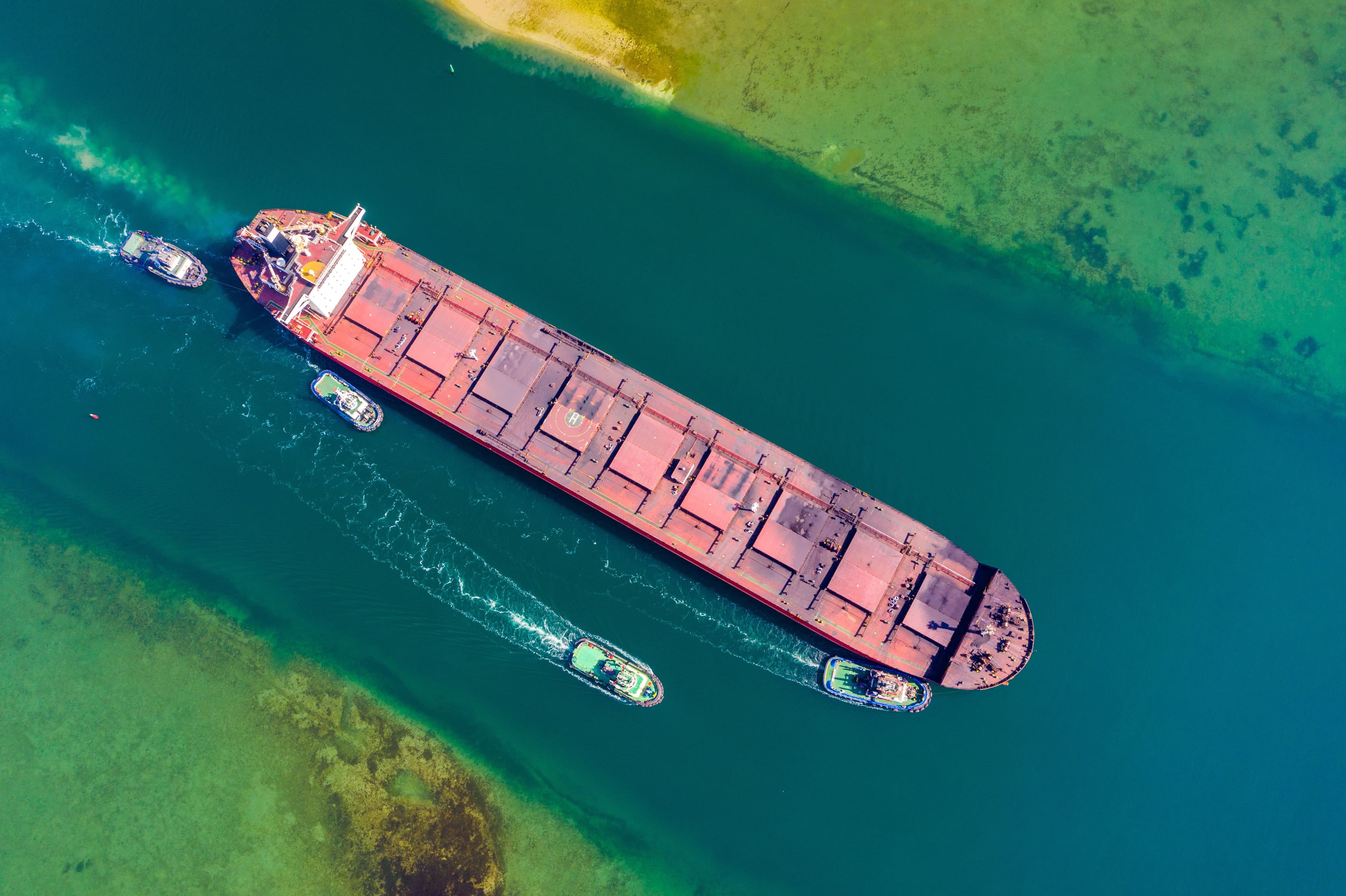 Tugs guiding a bulk carrier through a narrow channel, aerial view